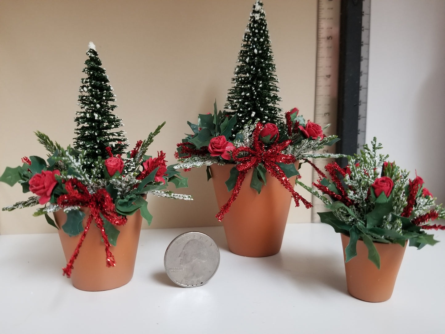Miniature christmas arrangement in terra cotta pots with red roses and red bow accents.